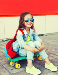 Portrait of little girl child with skateboard and backpack on city street