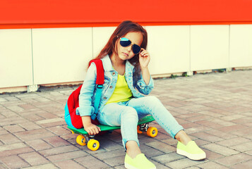 Portrait of little girl child with skateboard and backpack on city street