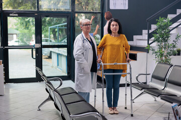 Portrait of doctor doing physical therapy exam with injured patient, supporting with walking frame...