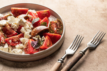 Salad with tomatoes, feta cheese and bazil leaves and forks for dinner with copy space on beige background