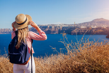 Traveler woman admires Santorini island, Greece enjoying sea landscape. Happy hiker with backpack...