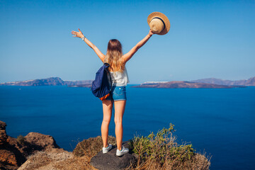 Woman traveler raised arms feeling happy looking at Caldera on Santorini island, Greece. Tourism,...