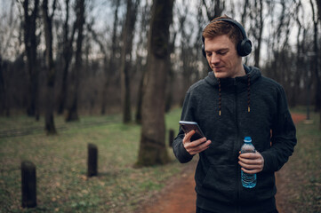 Redhead young man using a smartphone while running in the forest