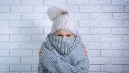 Lady with problem central heating. A young frustrated woman in woolen scarf freezing in a flat with cool temperature. A concept of heating crisis in the world.