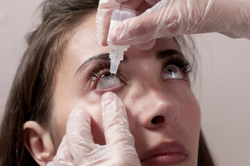 Close-up attentive optometrist dripping eye drops into the patient's eyes. Optometrist during an...