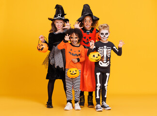 Happy Halloween! Kids in carnival costumes and makeup make a terrible gesture on bright colored yellow background