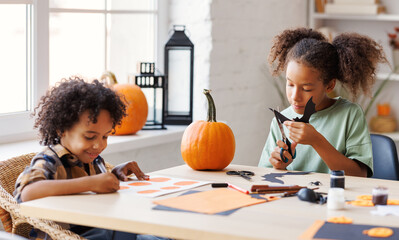 Happy ethnic children girl and boy making Halloween home decorations together