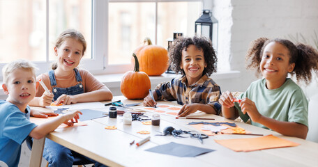 Happy multinational group of children making Halloween home decorations together
