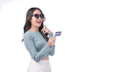 Excited asian woman wear sunglasses showing credit card in hand standing on white background. Cheerful surprised young girl holding blank card for payment online over isolated. Finance shopping online