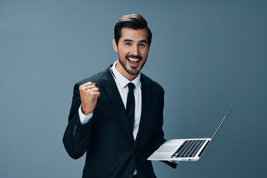 Man business looks into laptop and works online smiling fist up online in business suit video call business negotiations win on gray background copy place