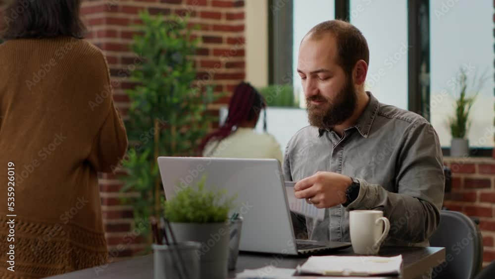 Poster company employee analyzing charts on documents and laptop, using research information to create busi
