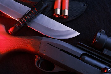 Weapon on black cloth: flashlight, knife, rifle, shells,top view. Top view of knife, rifle, shells.