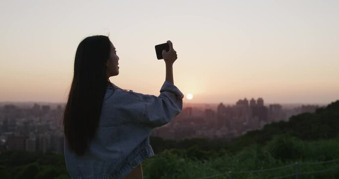 Woman take photo on cellphone under sunset