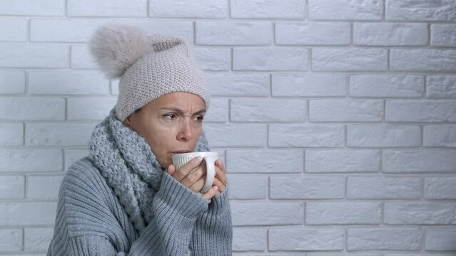 Lady with flu in unheating room. A sick woman in winter clothes try to get warm with hot bevarage in cold room during winter heating crisis.