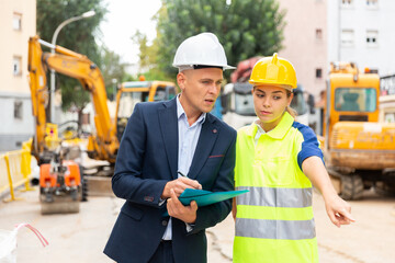 Civil engineers checking work process in construction site outdoors, comparing to blueprints