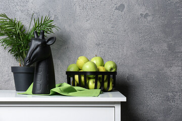 Stylish decor, basket of apples and houseplant on white table near grey wall indoors, space for text. Interior design