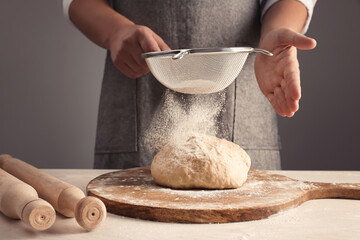 Man sprinkling flour over dough at table near grey wall, closeup - Powered by Adobe