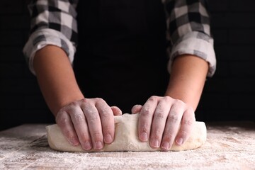 Man kneading dough at wooden table on dark background, closeup