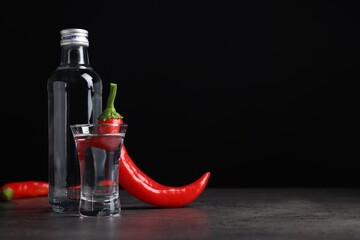 Red hot chili peppers and vodka on grey table against black background, space for text