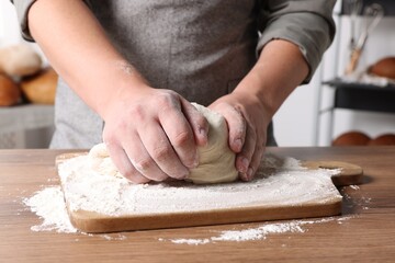 Man kneading dough at table in kitchen, closeup