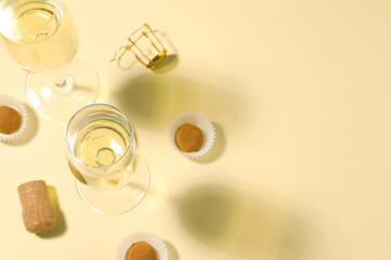 Glasses of delicious sparkling wine and chocolate truffles on light yellow background, above view....