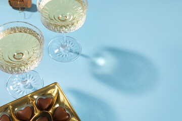Glasses of expensive white wine and heart shaped chocolate candies on light blue background. Space for text
