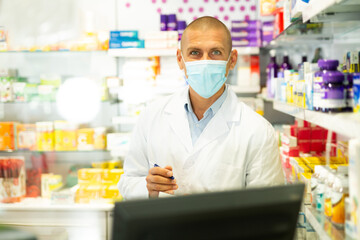 Portrait of pharmacist in medical mask working at the cash register in a pharmacy