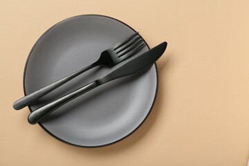 Grey ceramic plate with cutlery on pale orange background, top view. Space for text