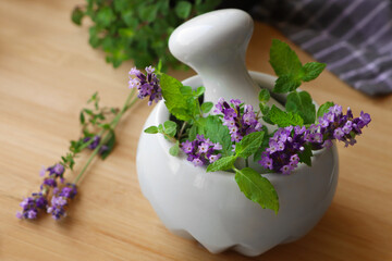Mortar with fresh lavender flowers, mint and pestle on wooden table, closeup