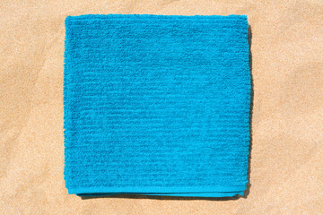 Fototapeta na wymiar Soft blue beach towel on sand, top view