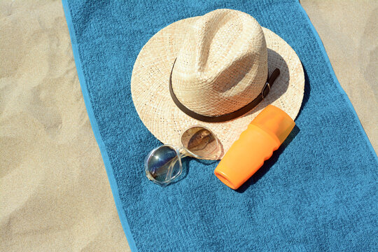 Soft Blue Towel, Sunglasses, Straw Hat And Bottle Of Sunblock On Sandy Beach