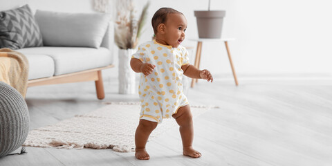 Cute little African-American baby learning to walk at home