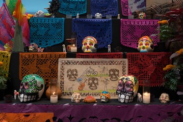 Colorful and painted day of the dead skulls, calaveras on an altar with papel picado, lighted candles and flowers