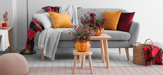 Grey sofa with autumn pumpkins and beautiful bouquets of flowers in living room