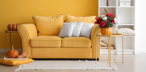 Yellow sofa with autumn pumpkins and beautiful bouquet of flowers in living room