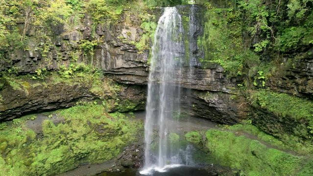 Low altitude drone view of a spectacular waterfall in a forest (Henrhyd Falls)