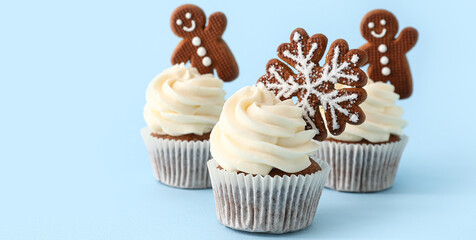 Tasty Christmas cupcakes with gingerbread cookies on light blue background