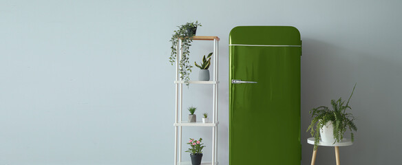 Stylish retro fridge, shelf unit and table with houseplants near light wall. Banner for design