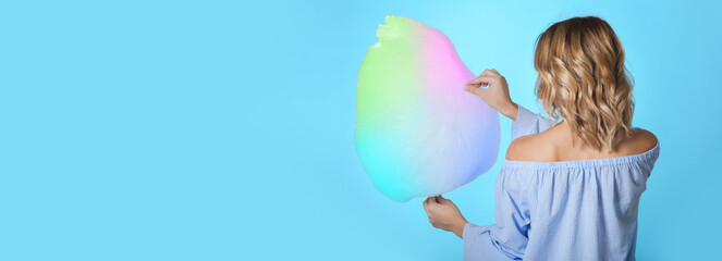 Young woman with tasty cotton candy on light blue background with space for text