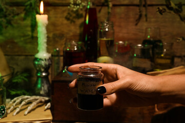 Witch holding jar with moon water on wooden background