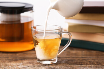 Pouring of milk from jug into glass cup on table