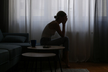 Young depressed woman sitting on the sofa next to the window