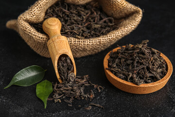 Bag, bowl and scoop with dry tea leaves on dark background