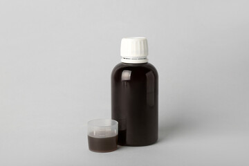 Bottle and cup of cough syrup on grey background