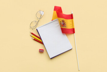 Notebook with stationery, eyeglasses and flag of Spain on yellow background