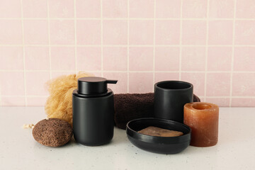 Bath accessories with candle on table near pink tile wall