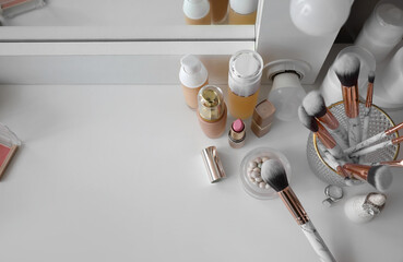 Holder with makeup brushes and decorative cosmetics on dressing table in room