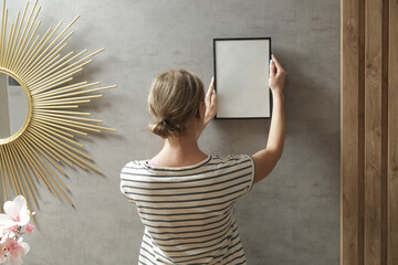 Woman arranging picture frames on wall in new house, diy home improvement concept	