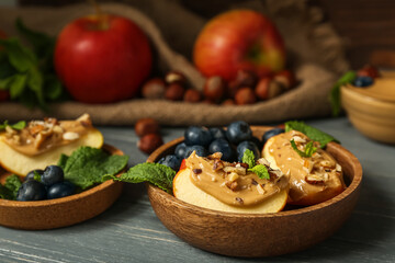 Bowls of tasty apple wedges with nut butter, blueberry and mint on dark wooden table, closeup