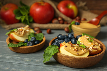 Bowls of tasty apple wedges with nut butter, blueberry and mint on dark wooden table, closeup
